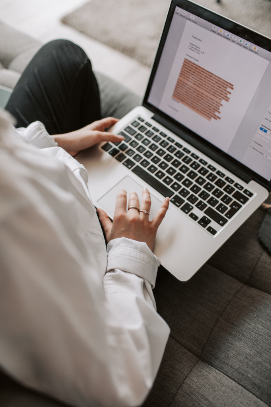 Female sits on sofa using a MacBook with a Word document open